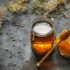 Honeycomb and transparent honey in a jar on a dark background with dry and fresh flowers.