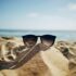 A pair of sunglasses at the sand with the sea in the background